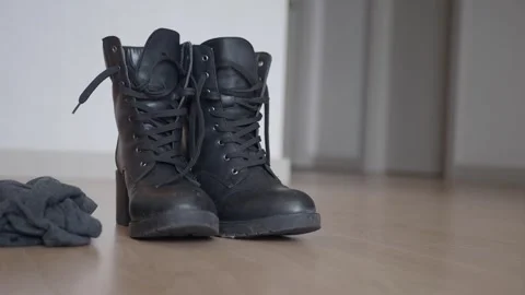A pair of stylish black boots is placed on the floor, complementing a casual Vídeos de archivo 285580252