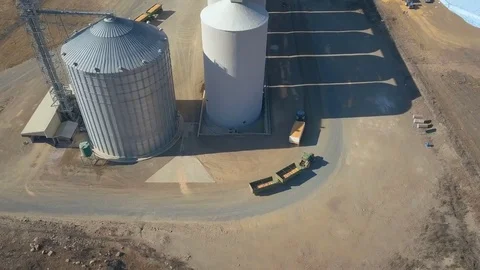 Pair of tractors pulling trailers with grain around silos aerial Video stock 79959425