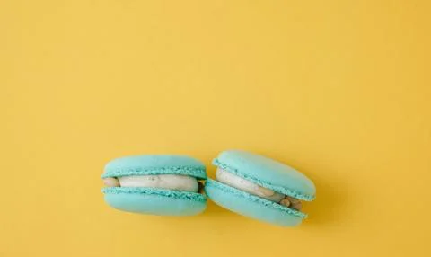 Pair of turquoise macarons on solid bright yellow background, vibrant contr.. Stock Photos