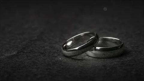 A pair of wedding ring bands on a dark stone background with floating bokeh e Vídeo Stock 106356733