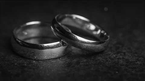 A pair of wedding ring bands on a dark stone background with floating bokeh a Vídeo Stock 106356816