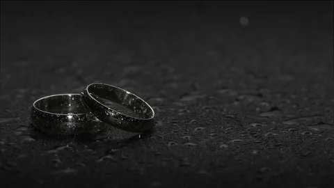 A pair of wedding ring bands on a water covered dark stone background with fl Vídeo Stock 106357334