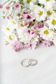 A Pair of wedding rings on a white surface with beautiful white and purple fl Stock Photos