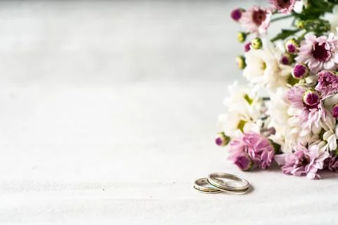 A Pair of wedding rings on a white surface with beautiful white and purple fl Stock Photos