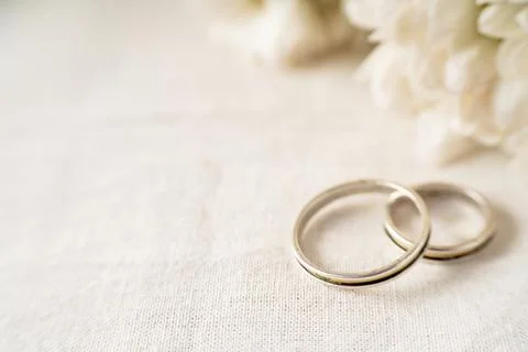 A Pair of wedding rings on a white surface with beautiful white flowers. Comm Stock Photos