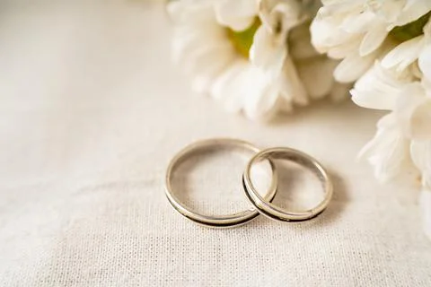 A Pair of wedding rings on a white surface with beautiful white flowers. Comm Stock Photos
