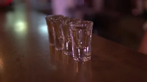 A pair of white hands begins putting shot glasses on the bar two at a time 動画素材 165845828
