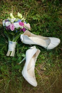 Pair of white ladies shoes on grass and beautiful bouquet of flowers Stock Photos