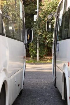 Pair of white minibuses aligned on paved path amid trees and urban elements Fotos Stock