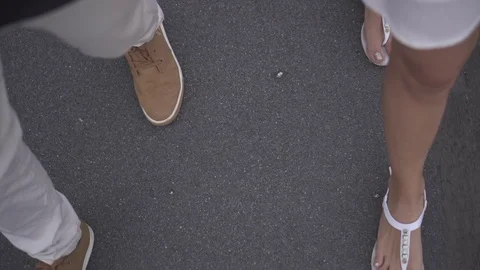 A pair in white sandals and brown sneakers walks along the sidewalk street Stock Footage 125613871