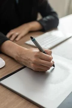 Pair of white woman's hands using computer pen on a wooden table Foto stock