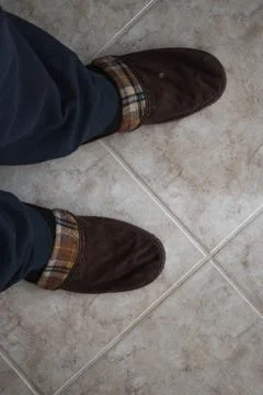 A pair of winter comfortable slippers over tiles floor. Man in warm slippers Stock Photos