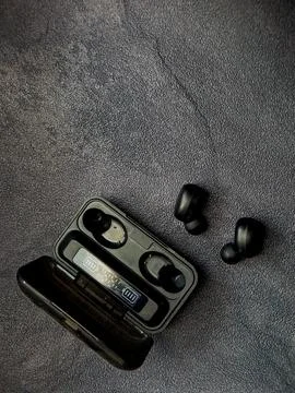 A pair of wireless earbuds rest beside their charging case on a textured gr.. Stock Photos