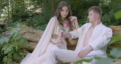 A pair of young lovers sit on a log in the garden Stock Footage 242854523