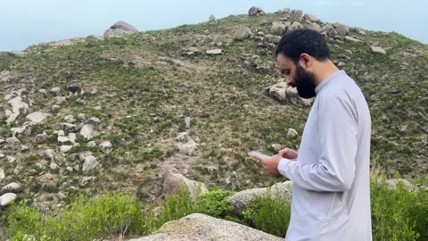 Pakistani Man in Traditional Clothes Scrolling Smartphone in Mountains Stock Footage 344440564