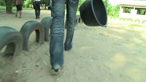 PAKRO YOUNG MAN CARRIES EMPTY CONTAINER PAST TIRE FENCE Stock Footage 58930453