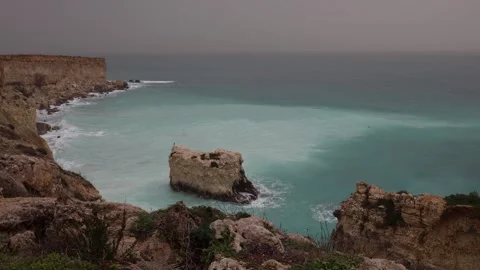 Pale turquoise bay with waves moving around a lone coastal rock Stock Footage 328286792