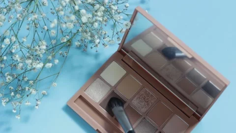 A palette of beige eyeshadows and brush on blue background, selective focus Stock Footage 142074797