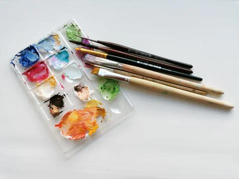 Palette with samples of multi-colored gouache paints and brushes after painti Stock Photos