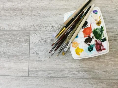 Palette with samples of multi-colored gouache paints and brushes after painti Stock Photos
