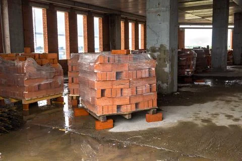 Pallets of bricks stand inside a monolithic frame building under construction Stock Photos