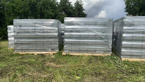 Pallets with gray concrete blocks wrapped in plastic film on a grassy site Stock Footage 341510305