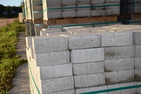 Pallets of grey paving blocks stored outdoors on grass before installation 库存照片