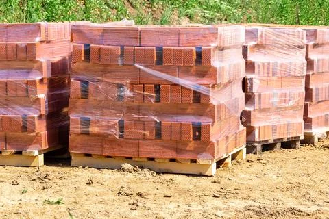 Pallets with new bricks stand at the construction site from which a layer of Stock Photos