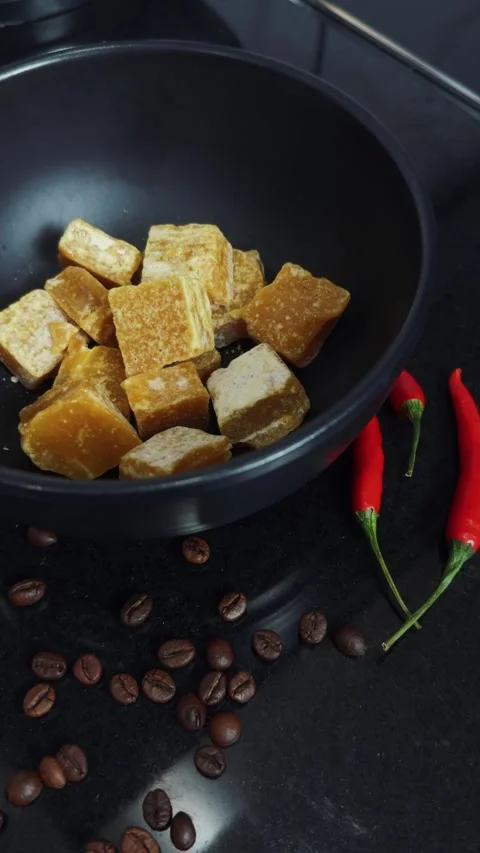 Palm sugar blocks in a dark bowl, scattered coffee beans, and red chili peppers Stock Footage 345515485