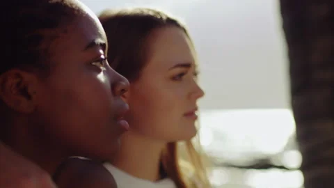 Palm tree in the foreground revealing profile of two young beautiful woman sitti Stock Footage 199457300