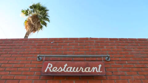Palm Tree Towers Over a Restaurant as a Sign Swings Stock Footage 61839737