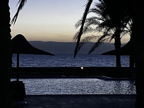 Palm trees and an infinity pool by the sea at dusk in Ras Sudr, Egypt Stock Photos