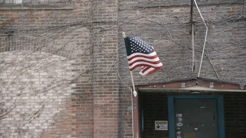 Pan across facade of industrial brick building with Flag Waving Stock Footage 89945048
