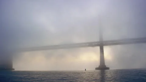 Pan across imposing Bay Bridge in fog at sunrise with morning commute traffic 스톡 동영상 242831178