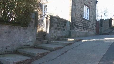 Pan across steps to stone cottage and zoom in to ancient village church Stock Footage 1097489