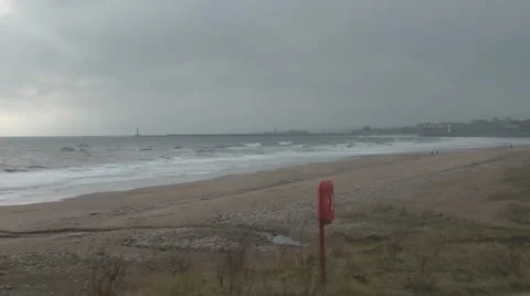 Pan across windy winter beach and back, lone walker on beach Stock Footage 1097566
