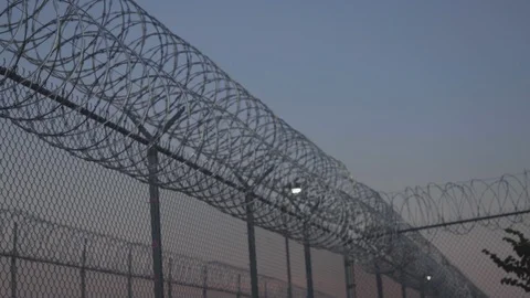 Pan Along Prison Razor Wire at Sunset Outside Jail 4K Stock Footage 114799921
