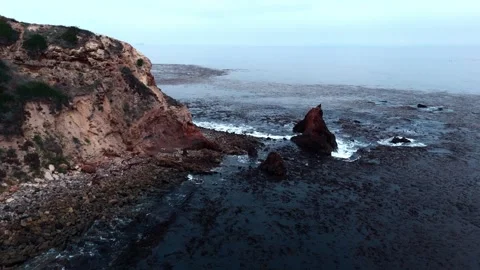 Pan up arial shot of waves hitting Rock cliff in an ocean 库存影片 250490208