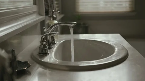 Pan back from hot water running in a sink Stock Footage 284953543