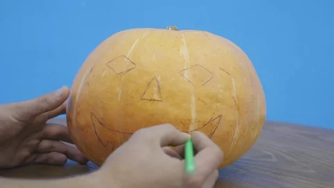 Pan of a boy drawing the Jack-o-lantern face on his halloween Pumpkin Stock Footage 81466499