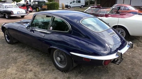 Pan: Dark blue Jaguar E-Type and other historic cars parking at oldtimer event Stock Footage 114449485