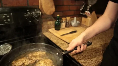 Pan down from arm to man's hand shaking and stirring a frying pan with meat 스톡 동영상 98368605