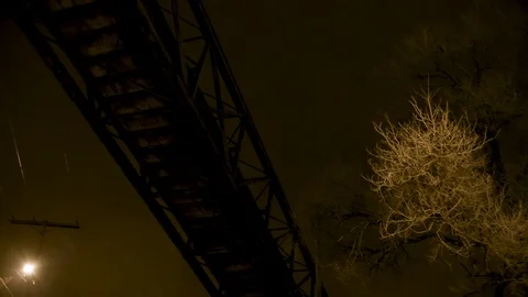 Pan down underside of bridge with barren tree and street lamp against night sky Stock Footage 89945486