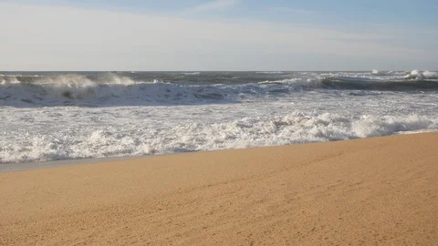 Pan up from empty, sandy beach to waves breaking on the shore Stock Footage 103288003