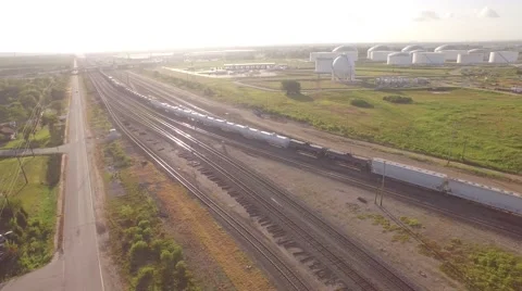 Pan Following Train Into Yard With Large Oil Storage in Background Stock Footage 61712123