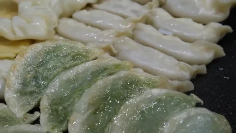 Pan-fried Chinese chive dumplings (Jiu Cai Jiao) being cooked on a flat grill pa Stock Footage 337374278
