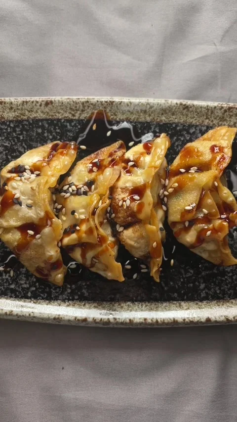 Pan-fried dumplings glazed with sesame sauce on speckled ceramic plate in light 库存影片 341661138
