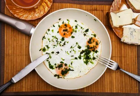 Pan of fried eggs, bacon with bread and tea on dark table surface, top view Stock Photos