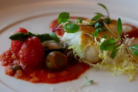 Pan fried white cod with tomatroes, tomato puree, olives and herb salad Stock Photos