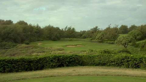 Pan of golf course putting green to ocean waves crashing onto rocks on shore Stock Footage 125336561